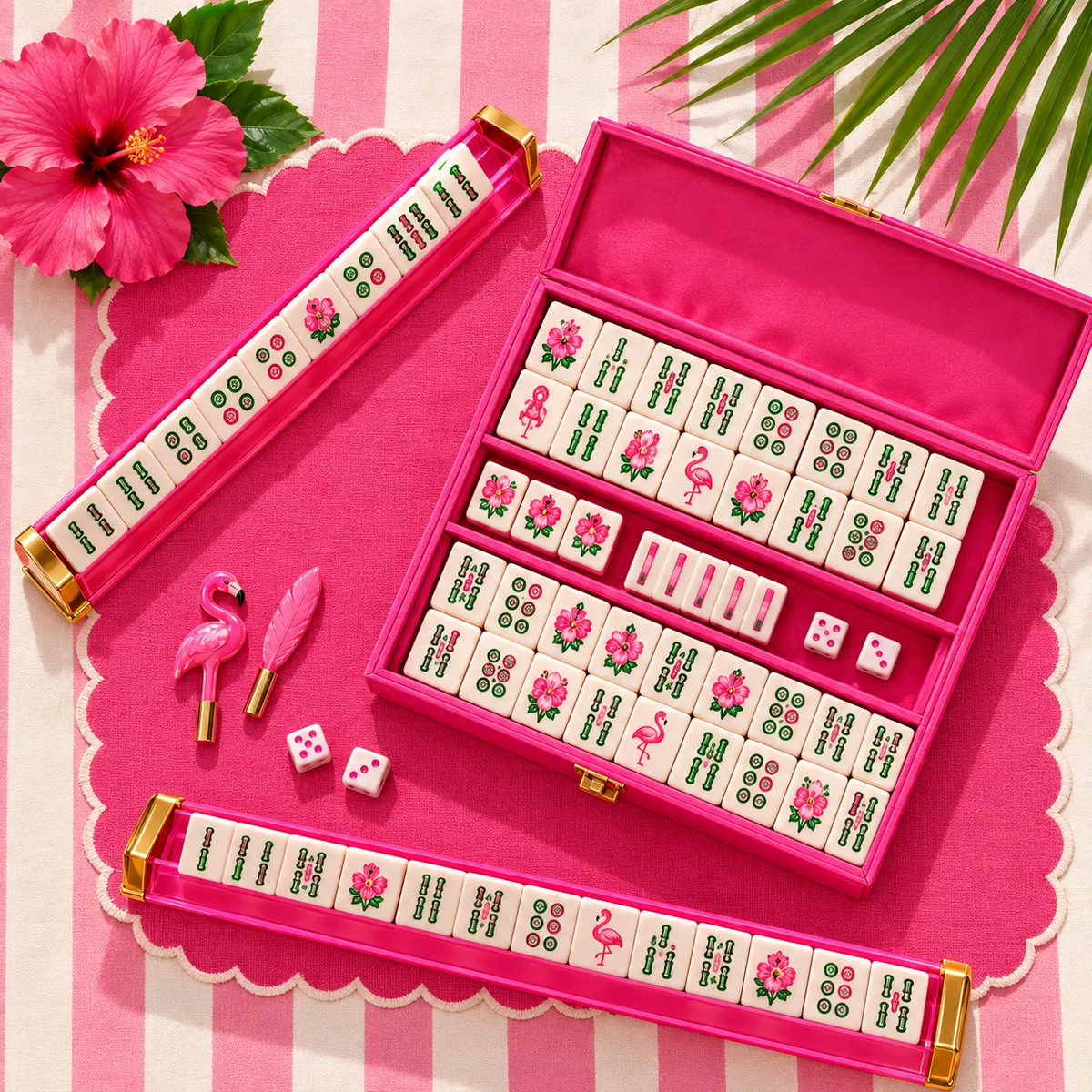 A pink mahjong set in an open case with pink racks, dice and a hibiscus on a striped tablecloth